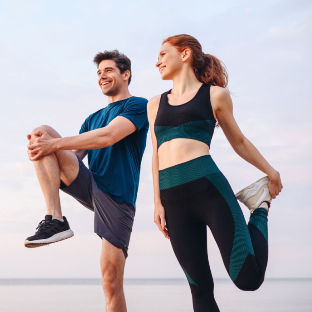 Happy couple stretching legs together during outdoor fitness workout session